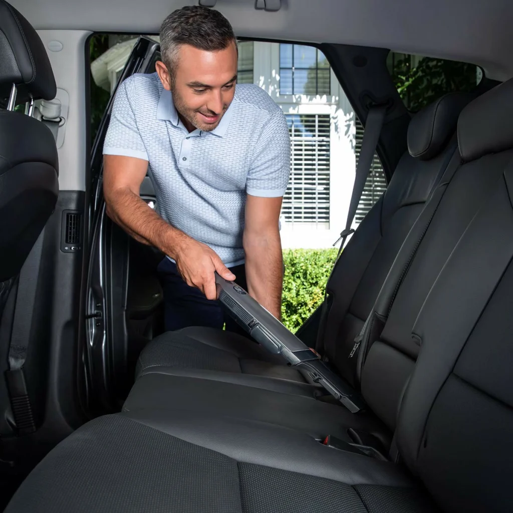 Un homme aspire les sièges de sa voiture avec le Shark WandVac