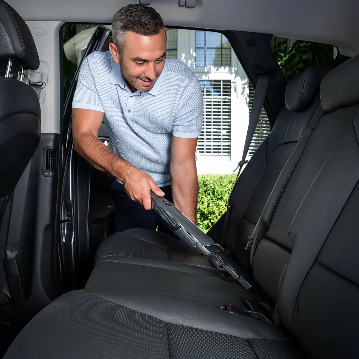 Un homme aspire les sièges de sa voiture avec le Shark WandVac